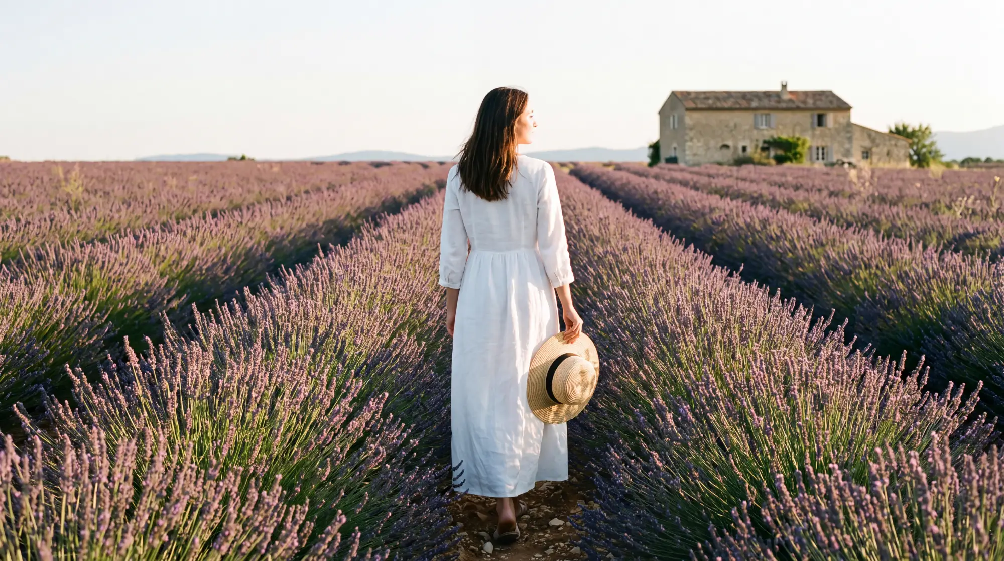 A woman in a white linen dress walking between rows of lavender on the Valensole plateau