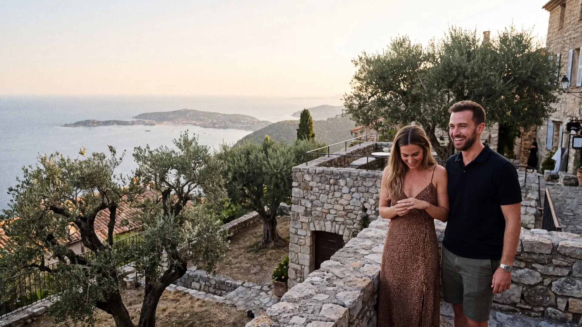 A couple on the stone terrace of a hilltop village just after the proposal, the sea far below